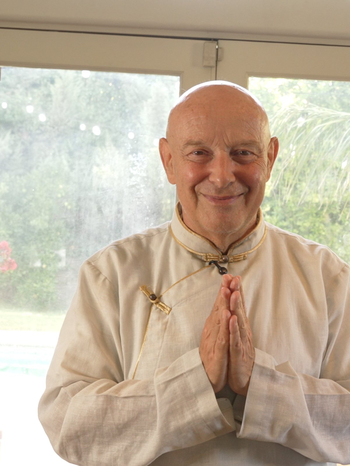 Michel Pascal standing at a glass door with his hands pressed together, smiling